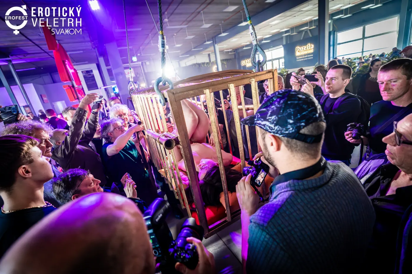 Spectators with cameras crowd close around a cage with a performer in the special zone