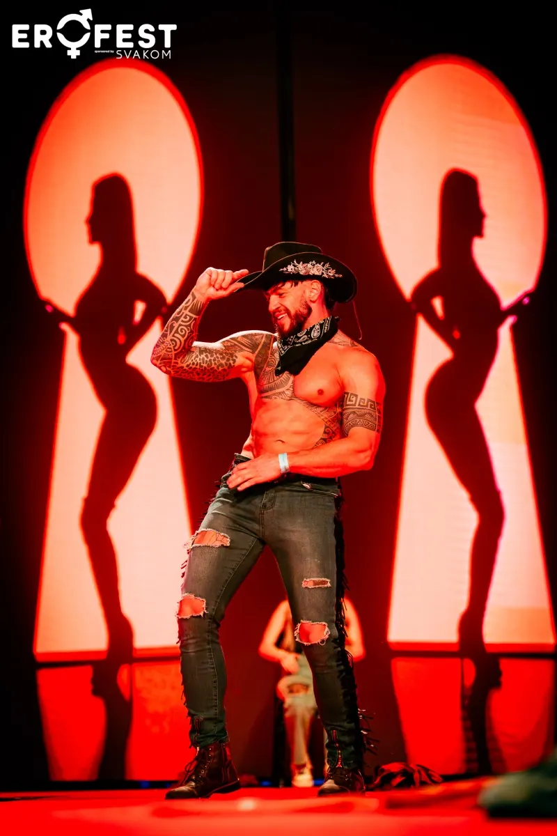 A stripper in a cowboy hat on the main stage among red silhouettes of dancers