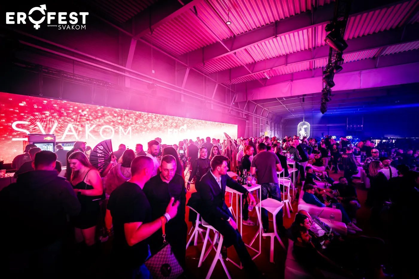 A lounge with bar tables in pink light next to the main hall